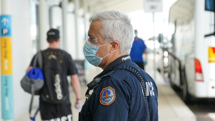 A police officer wearing a mask standing under a covered walkway near a bus