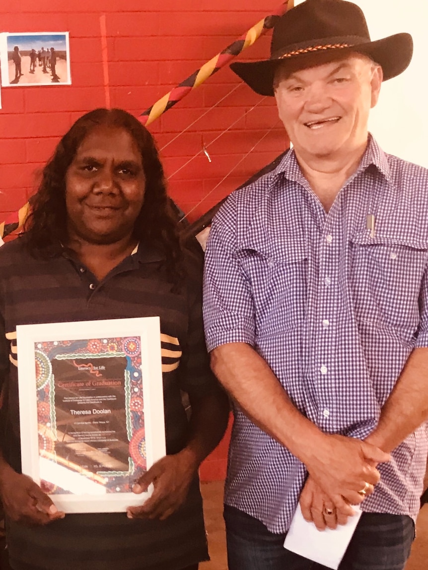 A man in a wide brim hat standing proudly next to an Aboriginal woman holding a certificate, smiling