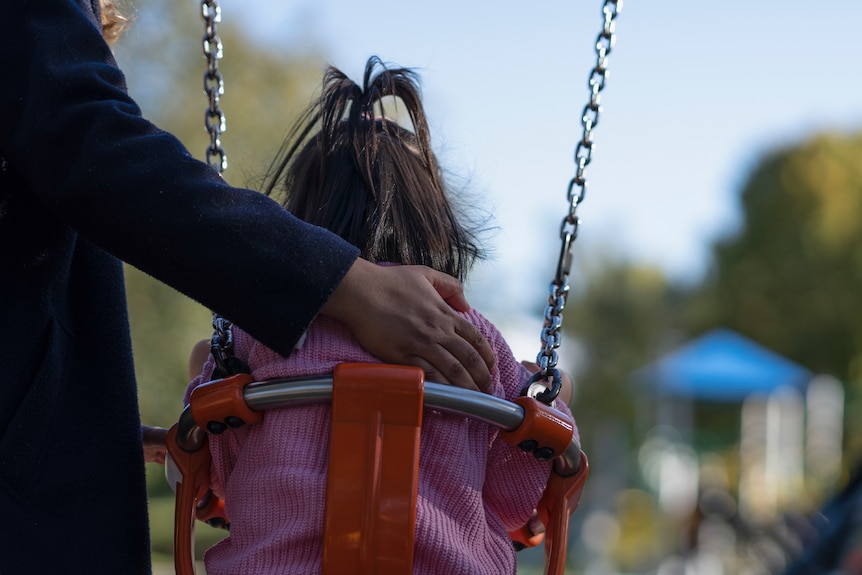 A woman pushes a child on a swing