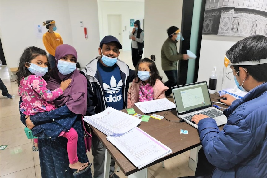 A family wearing a mask seeing a camera at a desk with a health worker.