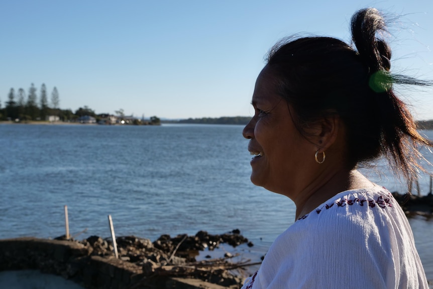 A woman stands looking out across a river.