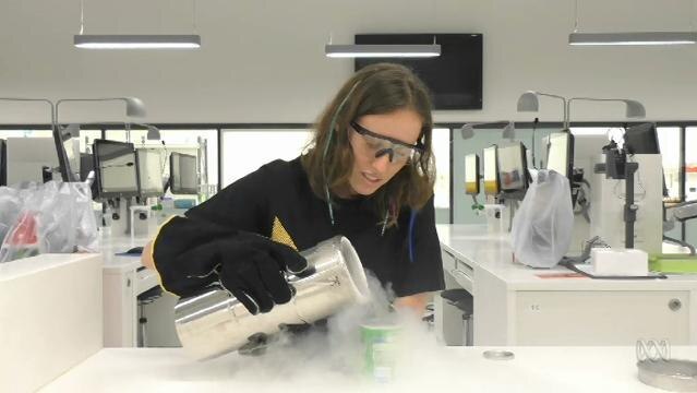 Woman pours liquid nitrogen from large container into smaller container in a laboratory
