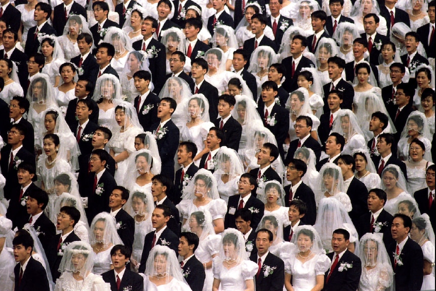 A crowd of men and women wearing traditional bridal attire all shout in unison