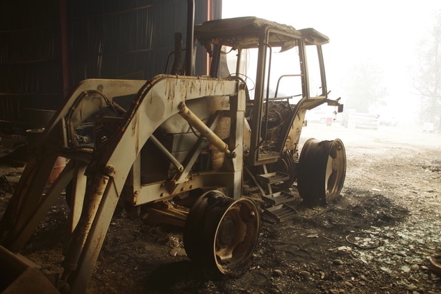 A burnt tractor sitting in a shed.