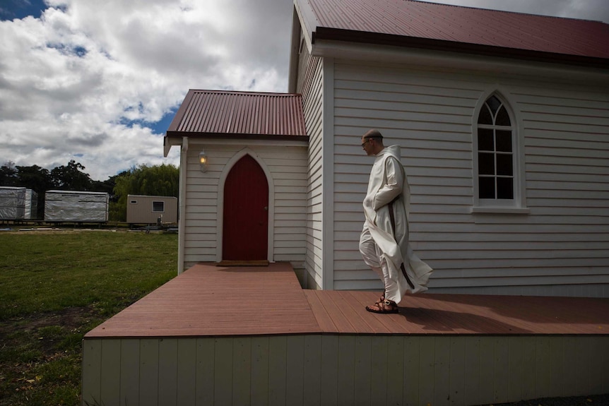 A Benedictine monk walks outside a small church.