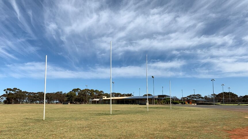 A green oval with white football goal posts under a blue sky.