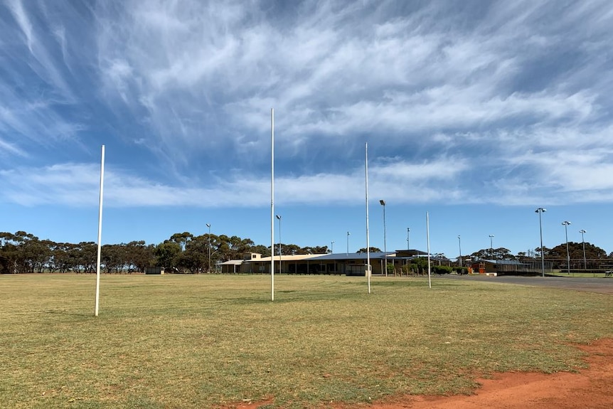 A green oval with white football goal posts under a blue sky.