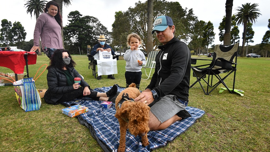 a group of people sit on a rug on the grass at a park