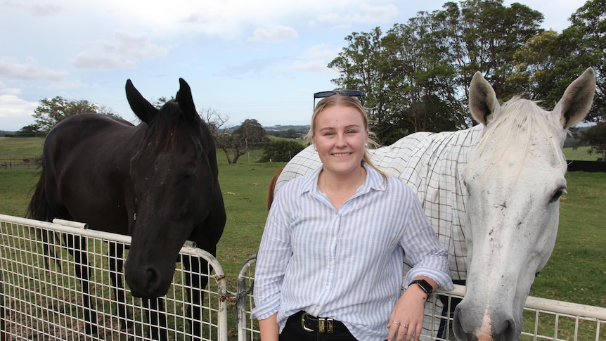 A smiling young woman with two horses behind her.