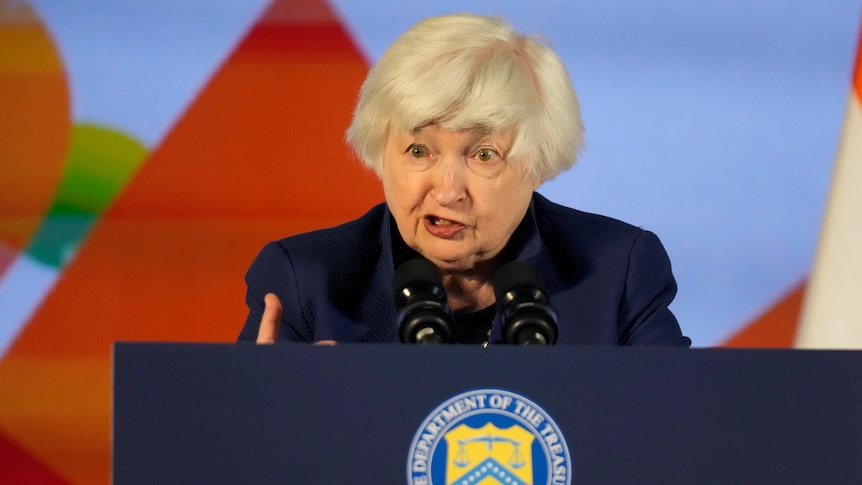 A woman stands at a podium and gestures with her hand. 