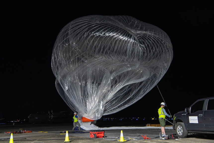 A transperant high-altitude balloon being prepared for launch at night.