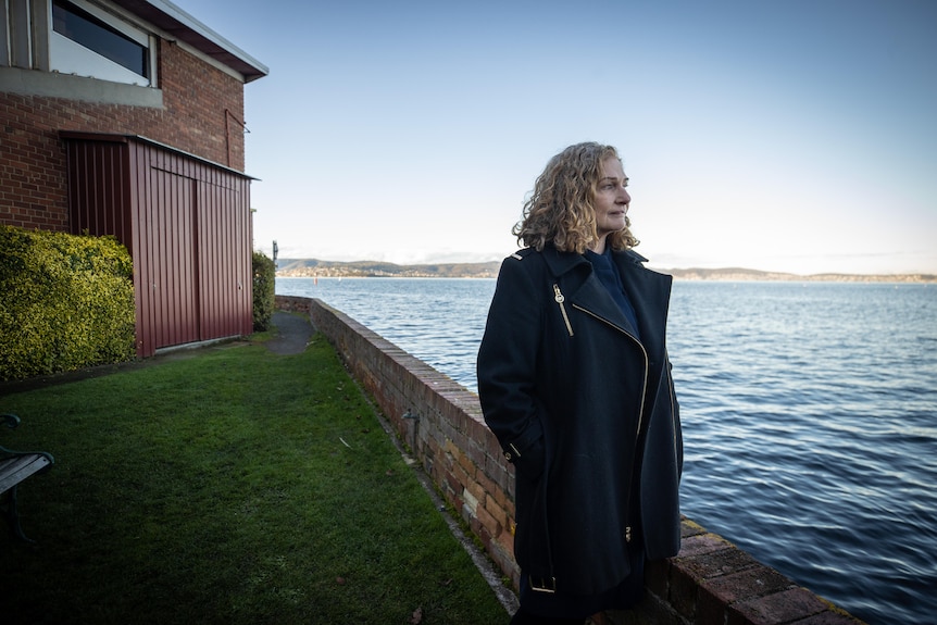 A woman wearing a dark coat looks over the water.