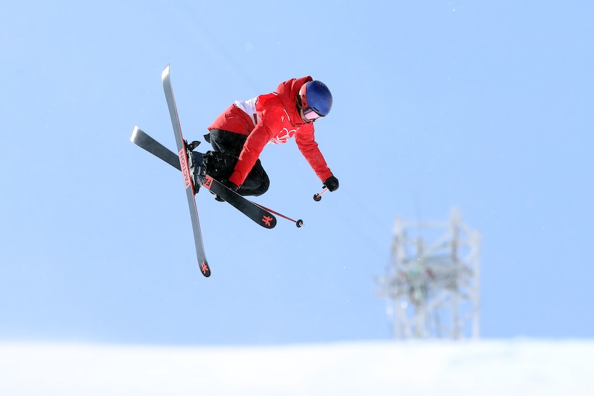 A skier in red does a trick with the blue sky as a background