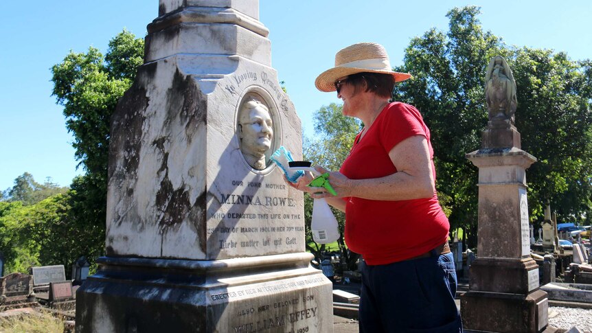 A woman cleans an ornate headstone in the South Brisbane cemetery.