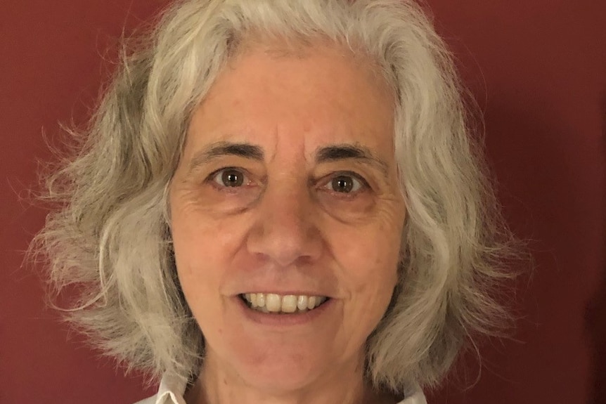 A woman with grey hair smiling against a red background.