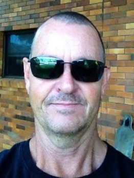 Stephen Lock wearing dark sunglasses and standing in front of a brick wall