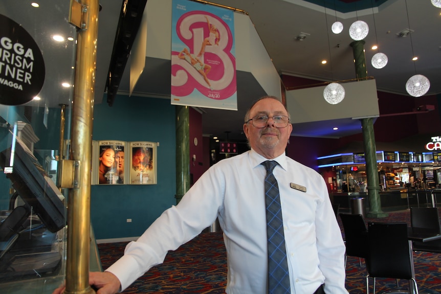 A man with a white shirt and tie stands in the foyer of a cinema.