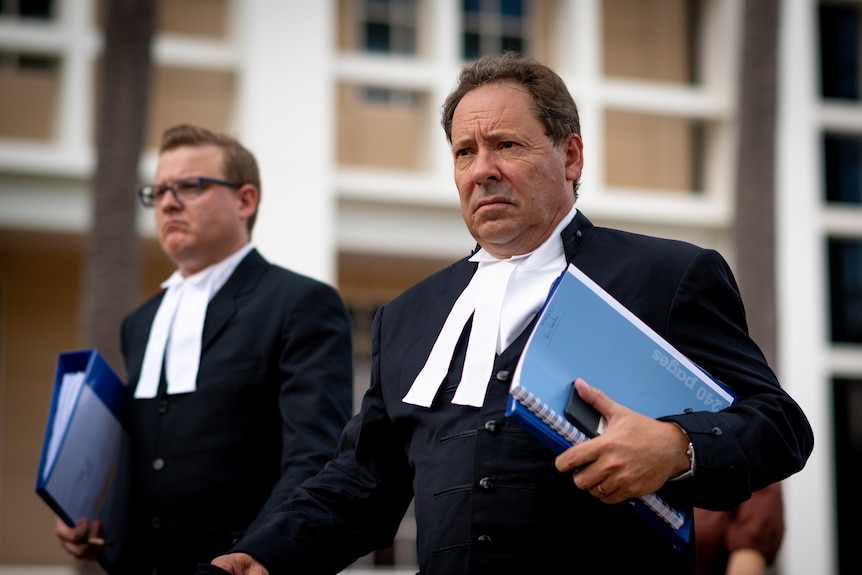 Two men carrying folders and wearing black barrister robes walk towards the NT Supreme Court.