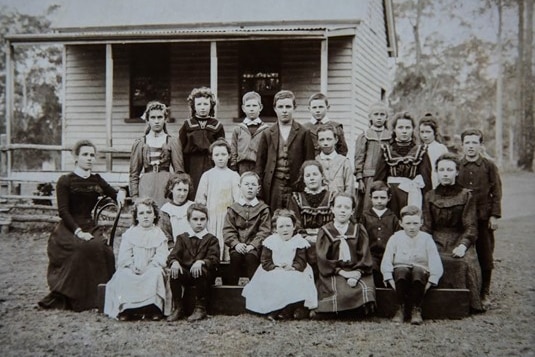 A black and white image of a school class and teacher in formal clothing taken around 1902.