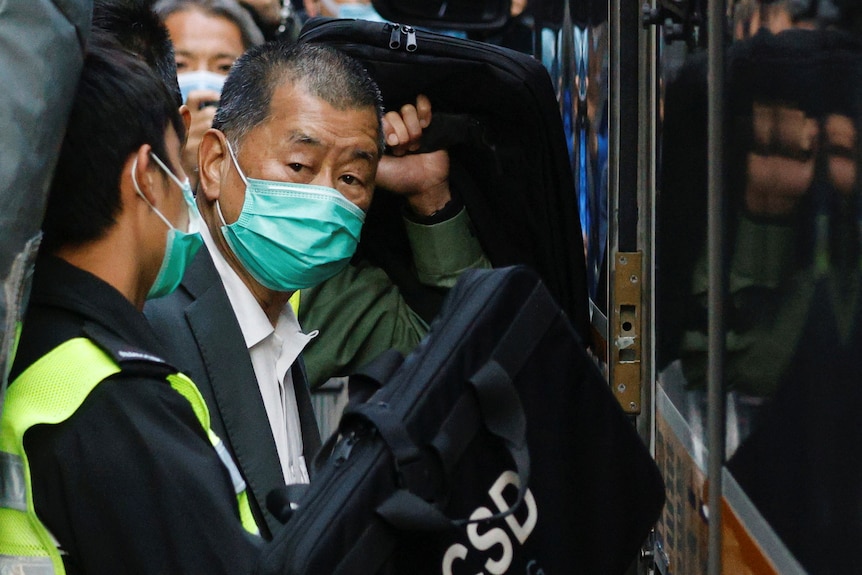 older asian man wearing a blue face mask looks at crowd as he boards van