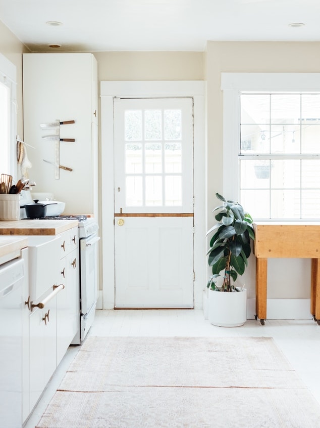 A clean, sparse white-walled kitchen with white cupboards and wooden floor to depict where the all-white house trend came from.