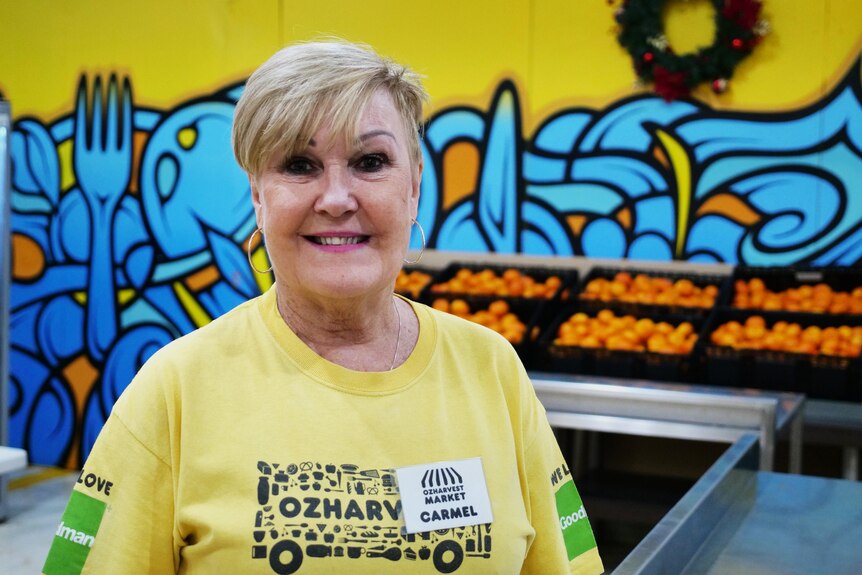 A woman with a yellow t-shire smiles in front of boxes of oranges
