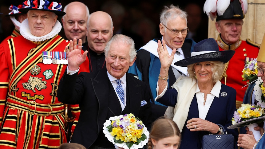 Charles and Camilla wave to onlookers as staff in royal costumes walk by them