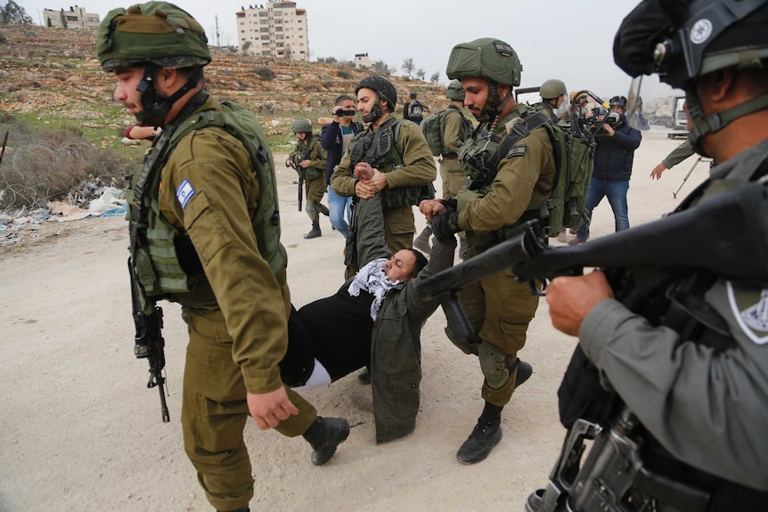 Israeli soldiers carry a man by his arms and legs.