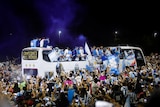 Crowds of people surround an open top bus which the players are on. 