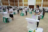 Volunteers check equipment and prepare ballot boxes spaced out in a large hall.