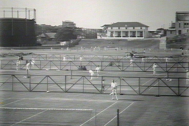 A number of tennis courts in front of a white clubhouse