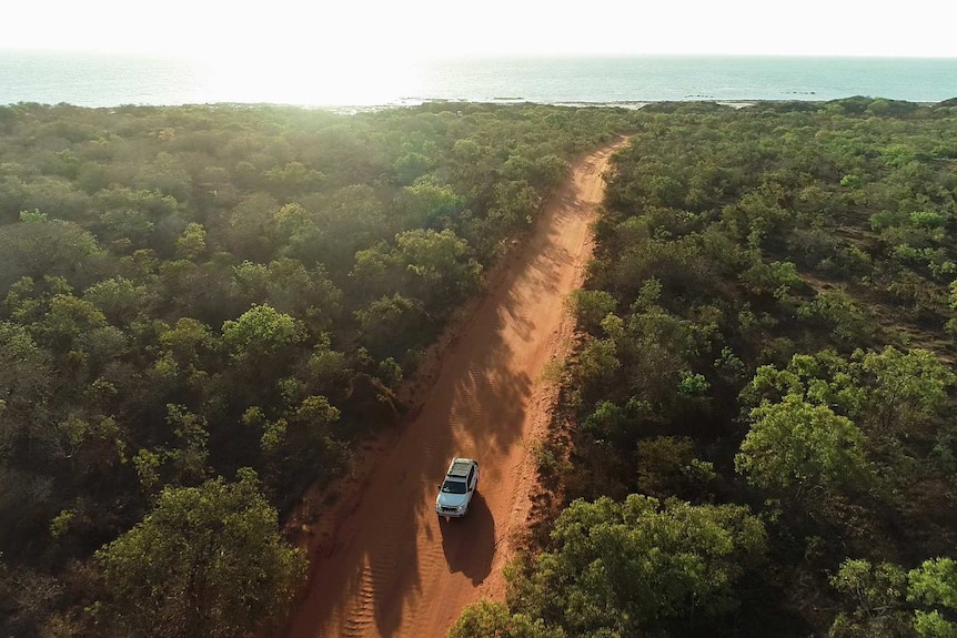 A car drives on a red dirt track.