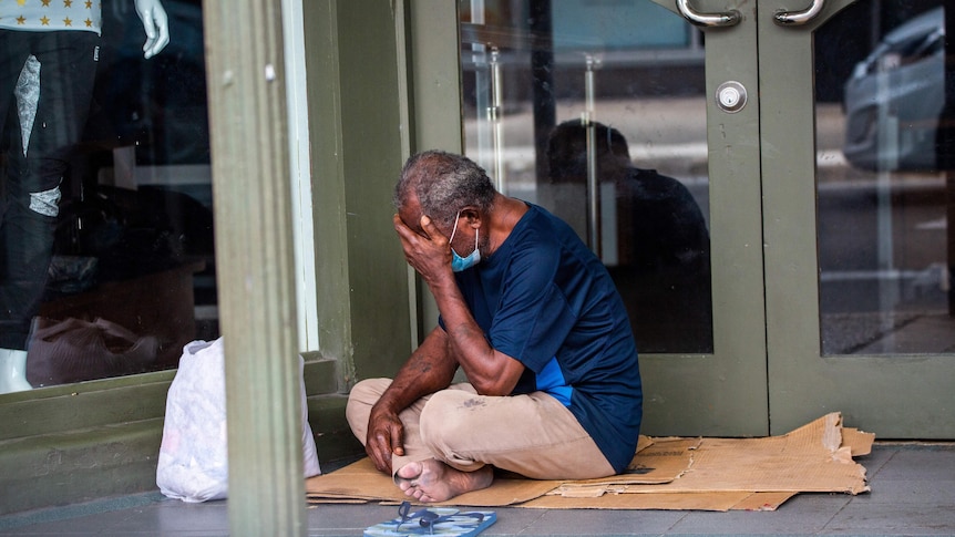 A man wearing a face mask sits on a road in Suva with his face in his hands. 