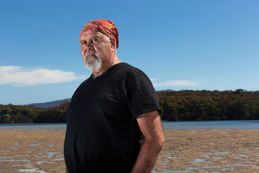 an Indigenous elder standing on mud flats looking off the frame pensively 