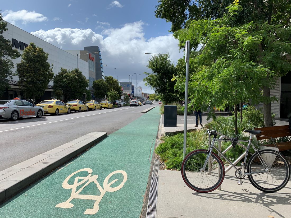 A bike locked in a bike rack beside a green bike lane on a city street.