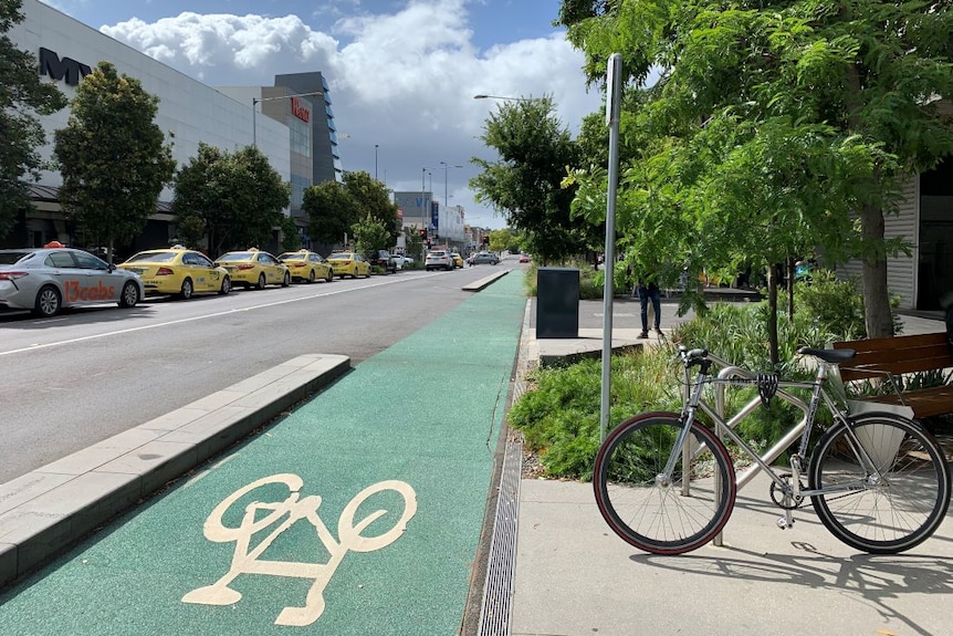 A bike locked in a bike rack beside a green bike lane on a city street.