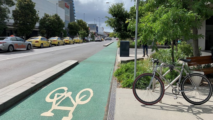 A bike locked in a bike rack beside a green bike lane on a city street.