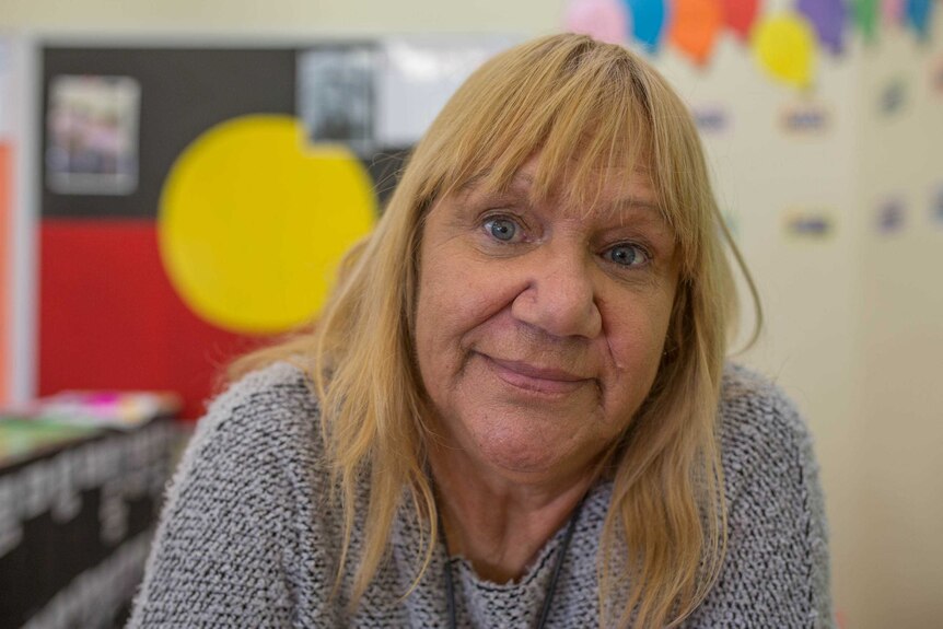 Geraldine Atkinson looks at the camera with an Indigenous flag in the background.