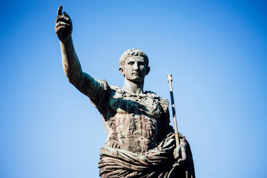 A statue of a Roman emperor against a blue sky.