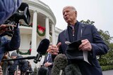 An older man with white hair in a navy suit speaks to a gaggle of reporters in front of the White House.