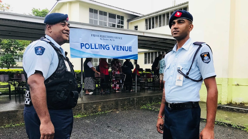 Two police officers stand in front of a yellow building and makeshift polling station in Suva.