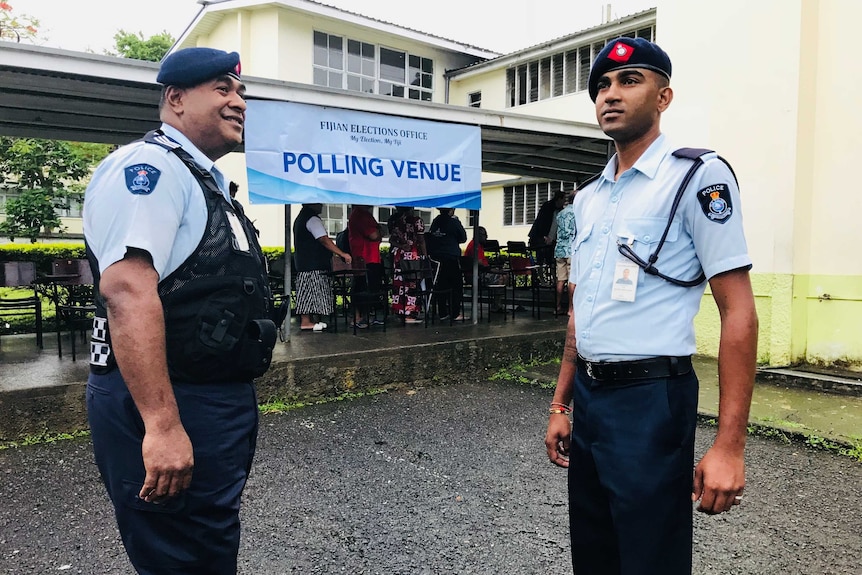 Two police officers stand in front of a yellow building and makeshift polling station in Suva.