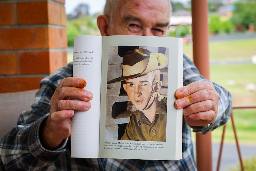 A close shot of Frank Hunt holding a book with a picture of him when he was 18 years-old