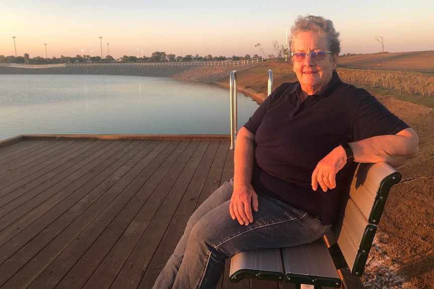 A woman sits on a bench beside a dam