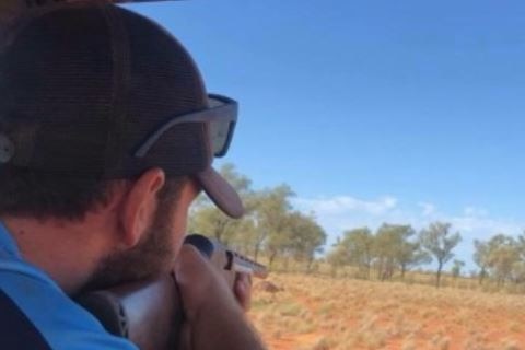 A man fires a gun at a kangaroo.
