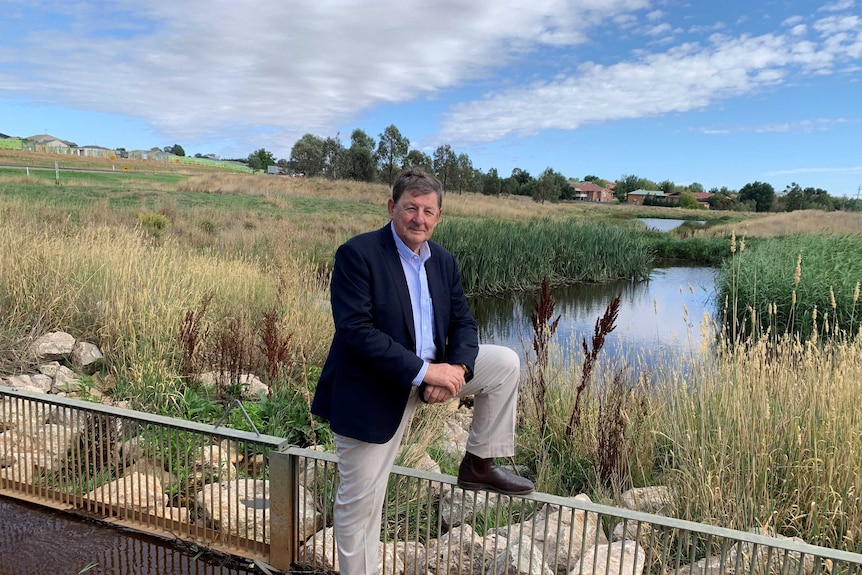 A man stands with one leg on a rail in a rural setting