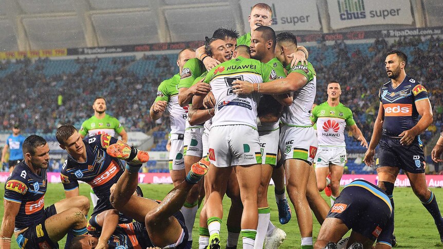 Rugby league teammates hug after a try while their opponents lie on the turf.