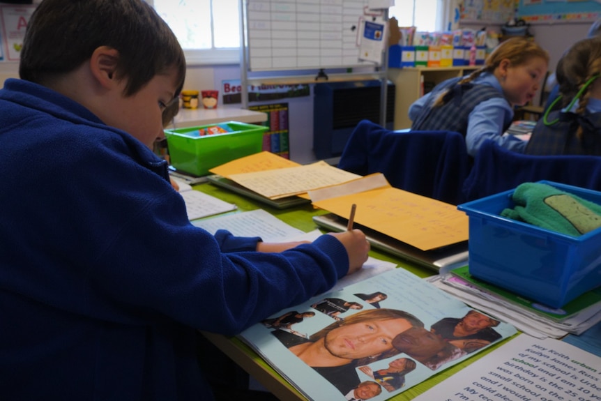 A primary school student in a classroom with pictures of Keith Urban on his desk