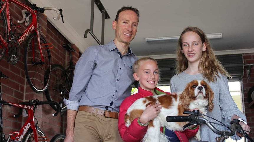 A man and two girls stand with their dog next to a bike.