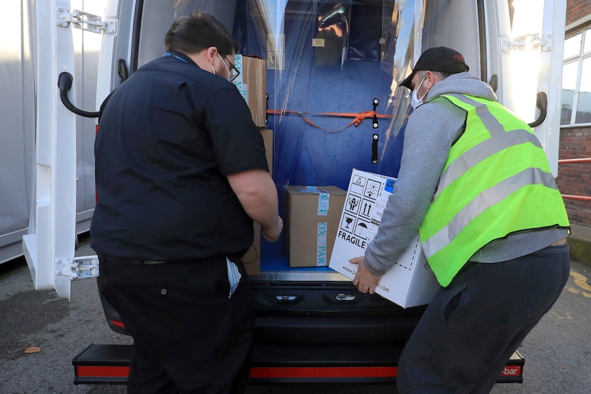 Pharmacy technician in a fluro vest at a van takes delivery of the first batch of COVID-19 vaccine